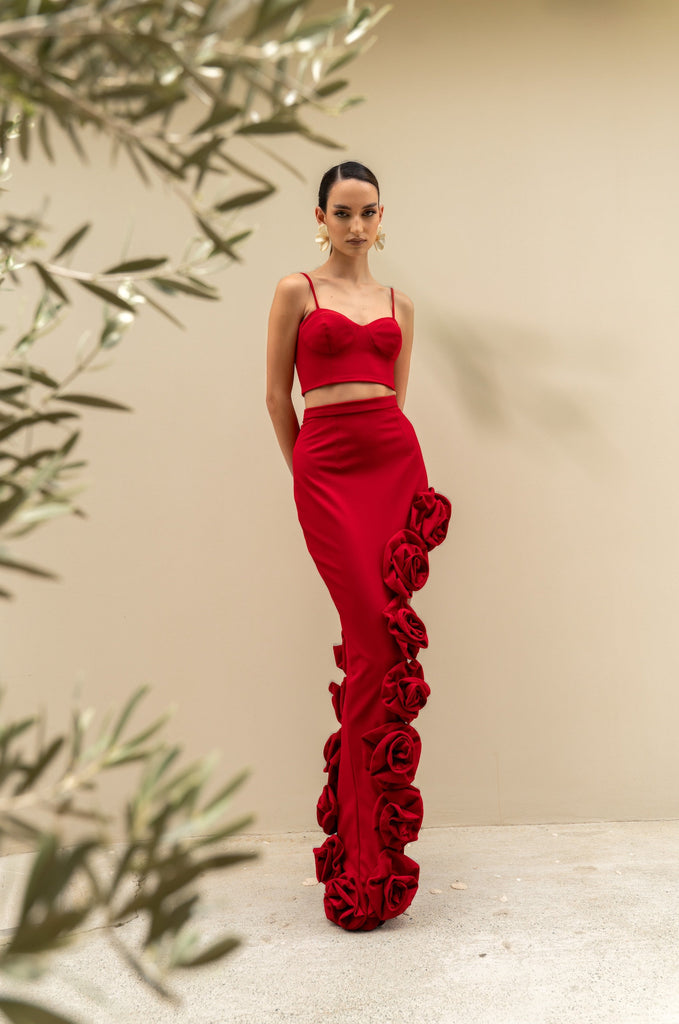 Joanna Economou Designs, @joannaeconomoudesign Cyprus-based fashion designer resort and luxury wear occasion two-piece set features structured bustier top and a high-waisted column skirt, with cascading handcrafted roses along the leg red crimson hue colour, elegant designer piece for women island Mediterranean-inspired. Shop online from Cyprus worldwide shipping.